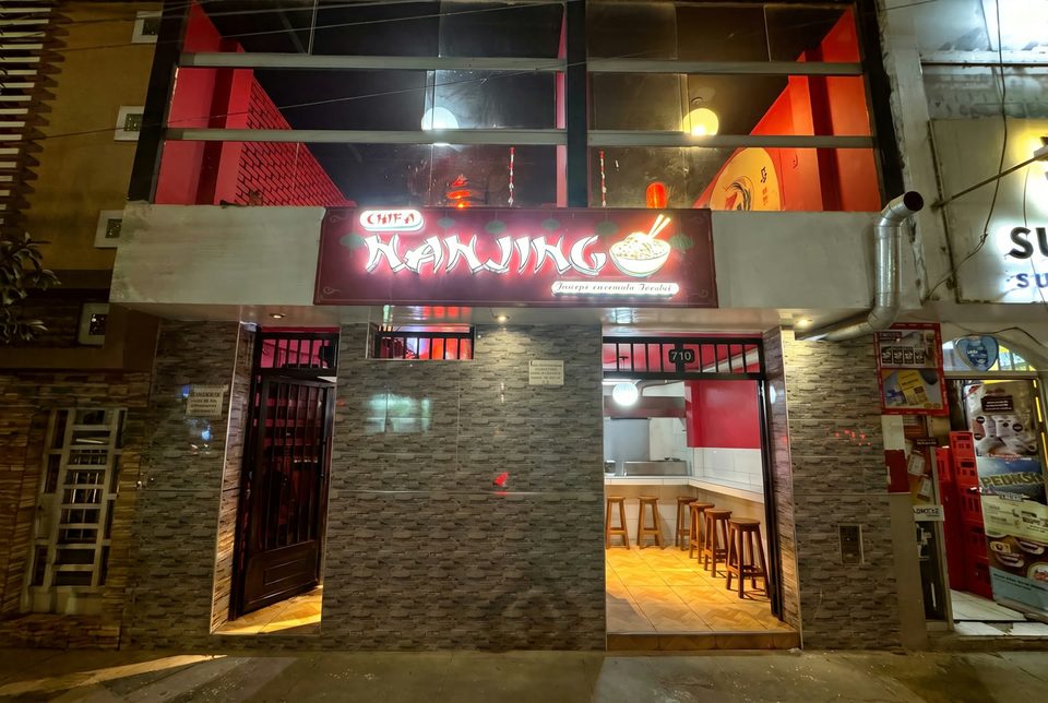 La fachada de Chifa Nanjing de noche, con su letrero rojo iluminado en la Av. Libertad 710