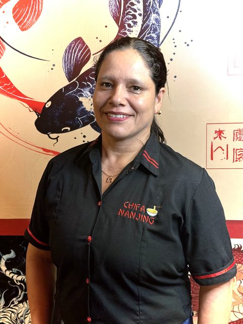La señora Mari, del equipo de Chifa Nanjing, con el uniforme del local frente al mural del koi